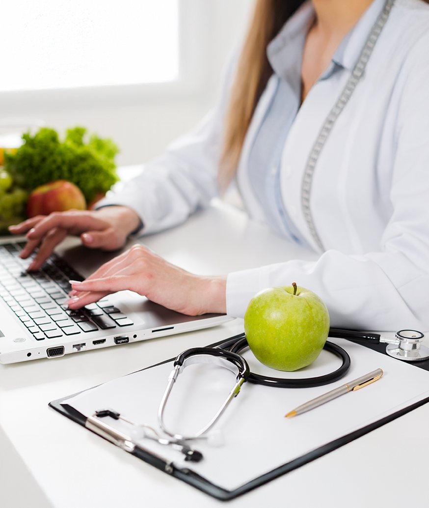 Nutricionista trabalhando no computador, com maçã e estetoscópio sobre a mesa