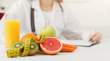 Nutritionist desk with healthy fruits, juice and measuring tape. Dietitian working on diet plan. Weight loss and right nutrition concept